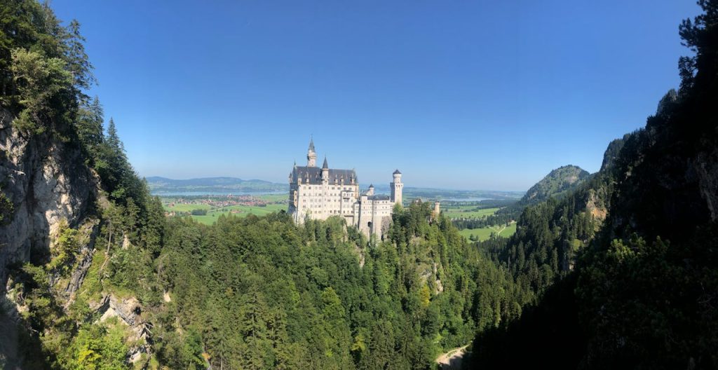 Panoramic view of Neuschwanstein Castle surrounded by lush greenery in summer.